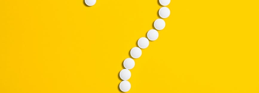 white pills arranged in the shape of a question mark on a bright yellow background