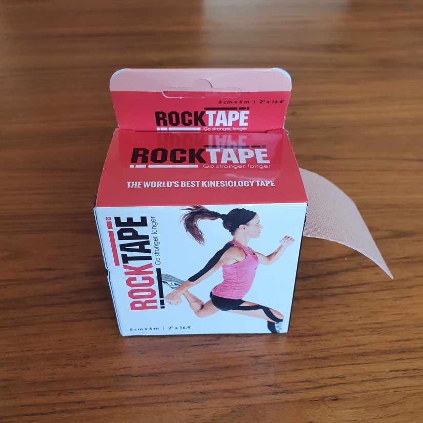 Box of Rock Tape kinesiology tape. Photo of a woman on the box with tape applied to her upper arm and upper leg